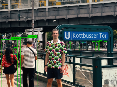 Homme portant la chemise Digital Camouflage à Kottbusser Tor à Berlin, entouré de piétons détectés par des cadres verts d'IA, lui n'étant repéré par aucun cadre.