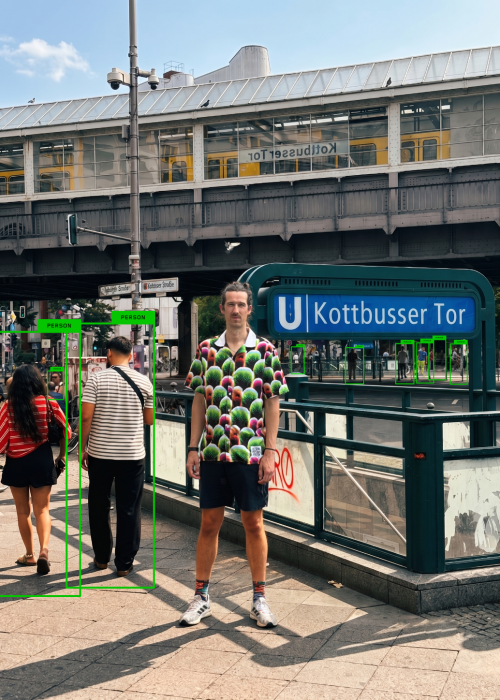 Homme portant la chemise Digital Camouflage à Kottbusser Tor à Berlin, entouré de piétons détectés par des cadres verts d'IA, lui n'étant repéré par aucun cadre.